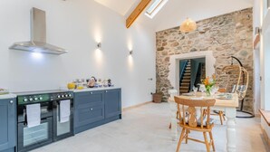 Eine Küche mit Herd, Backofen und blauen Schränken, ein Essbereich mit Tisch und Stühlen sowie eine Steinwand.
