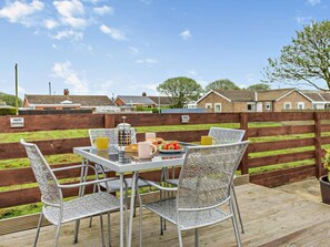 An outdoor patio with a table set for two, surrounded by metal chairs, a coffee pot, and a plate of fruit. - 2 Bed in Chathill (oc-86877) (Beadnell)