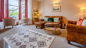 A living room with a sofa set, a coffee table, a patterned rug, and a painting on the wall. - 3 Bed in Keswick (oc-86867) (Keswick)
