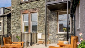 A stone building with a patio area featuring wooden chairs and a small table. - 3 Bed in Keswick (oc-86867) (Keswick)