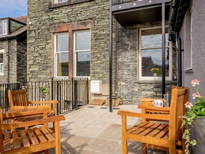 A stone building with a patio area featuring wooden chairs and a small table. - 3 Bed in Keswick (oc-86867) (Keswick)