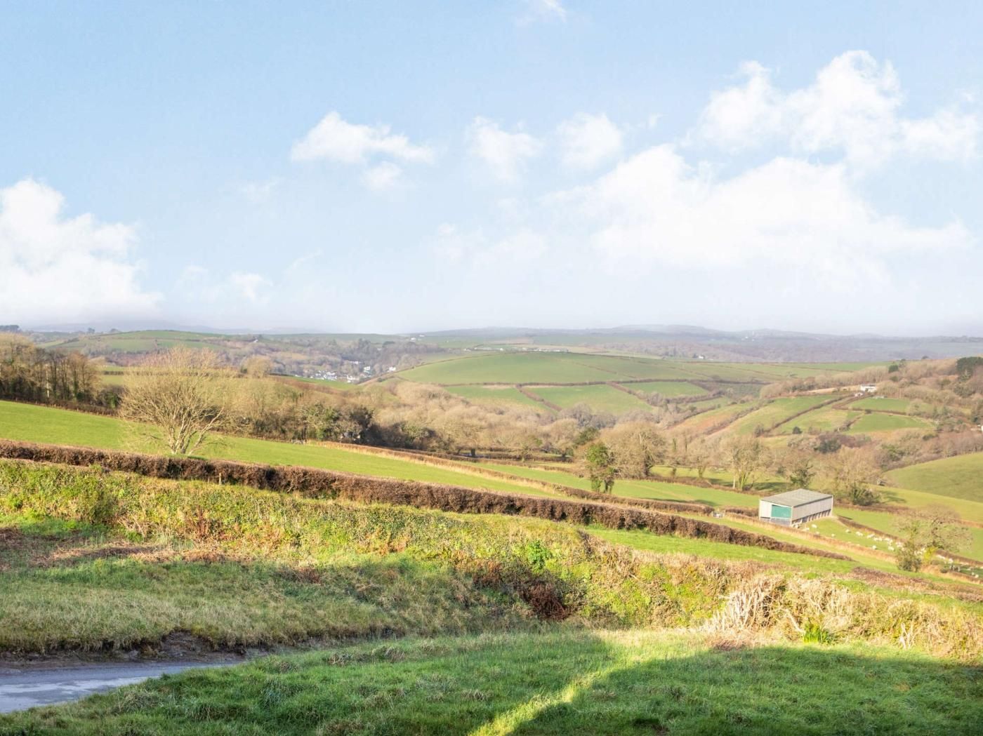 Un paysage rural caractérisé par des collines douces, un petit bâtiment et un ruisseau.