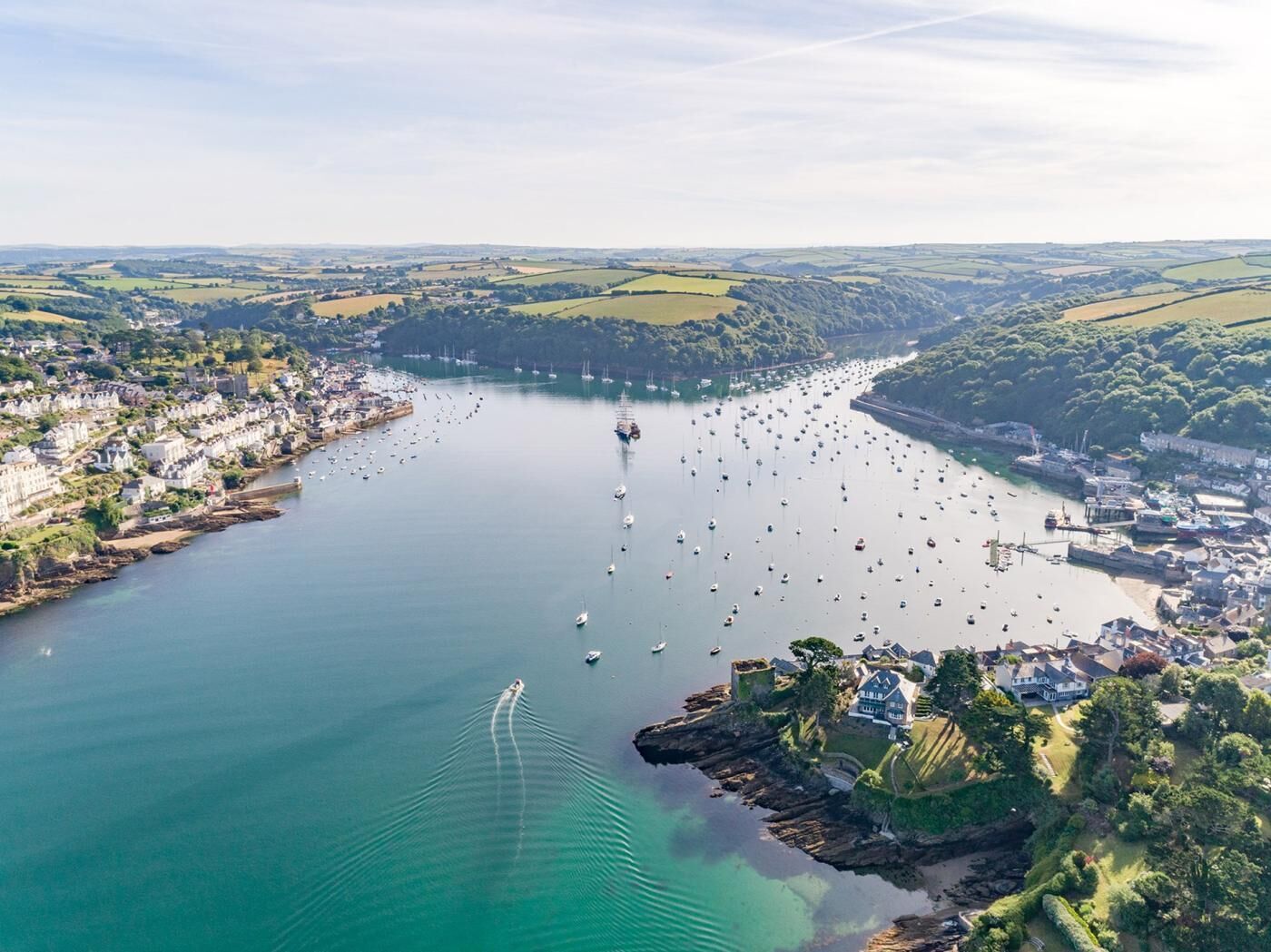 An aerial view of a coastal town with a marina filled with boats, surrounded by green hills and residential areas.