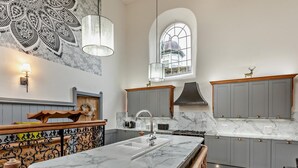 Una cucina con piani di lavoro in marmo, mobili grigi, un'isola centrale, una parete decorativa e una finestra con vista.