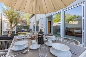 An outdoor dining area with a table set for four, a coffee pot, and a large umbrella. - 3 Bed in Barnstaple (oc-87116) (Fremington)