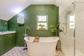 A bathroom with a freestanding bathtub, a glass shower enclosure, a window with plants, and green walls. - 3 Bed in Barnstaple (oc-87116) (Fremington)