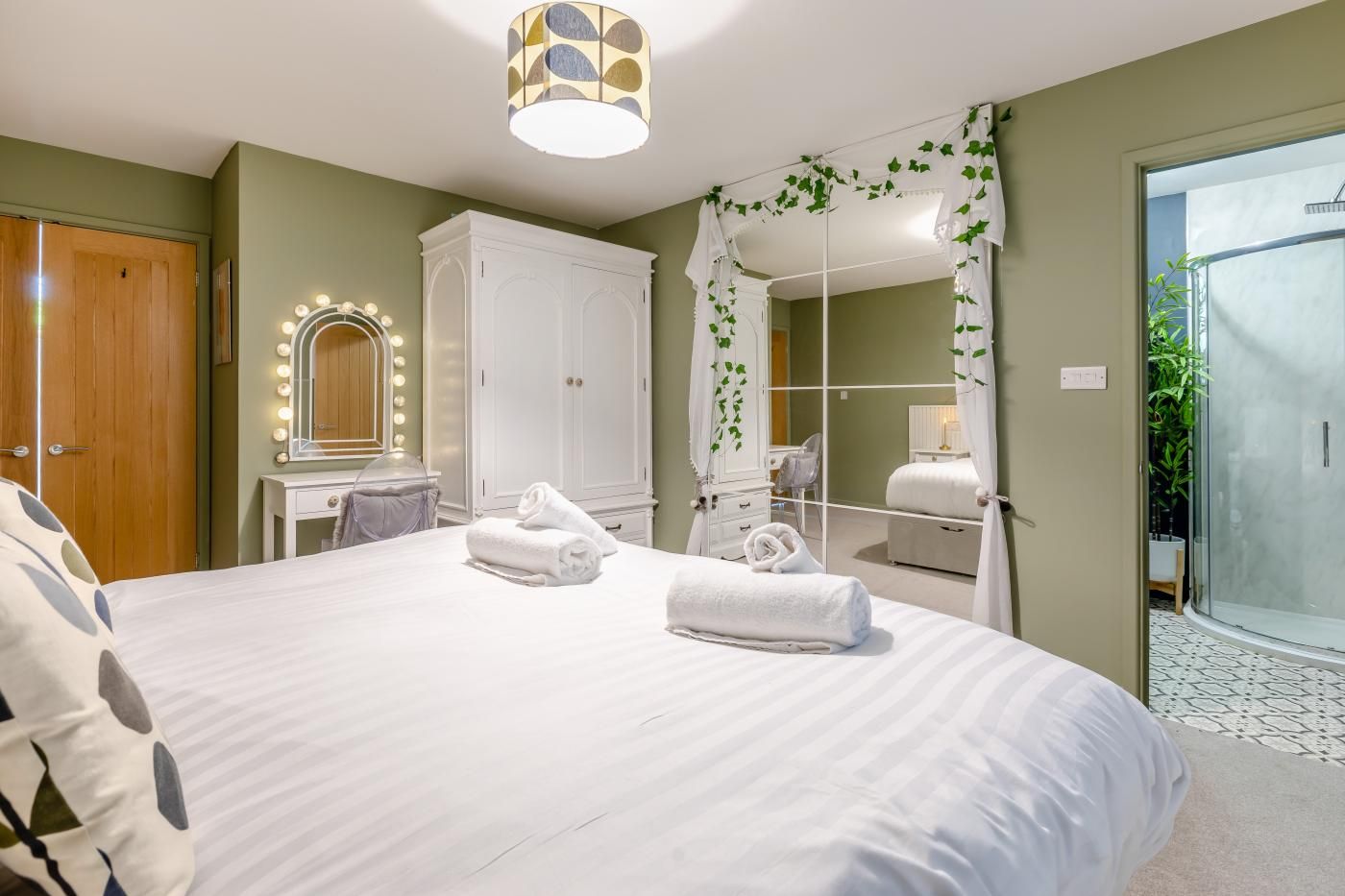Een hotelkamer met een groot bed, een kaptafel met spiegel, een kledingkast en een douche.
