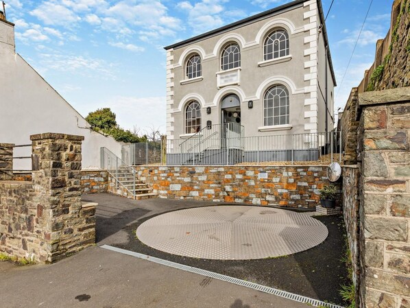 A building with a stone facade, a circular paved area, and a metal fence. - 3 Bed in Barnstaple (oc-87116) (Fremington)