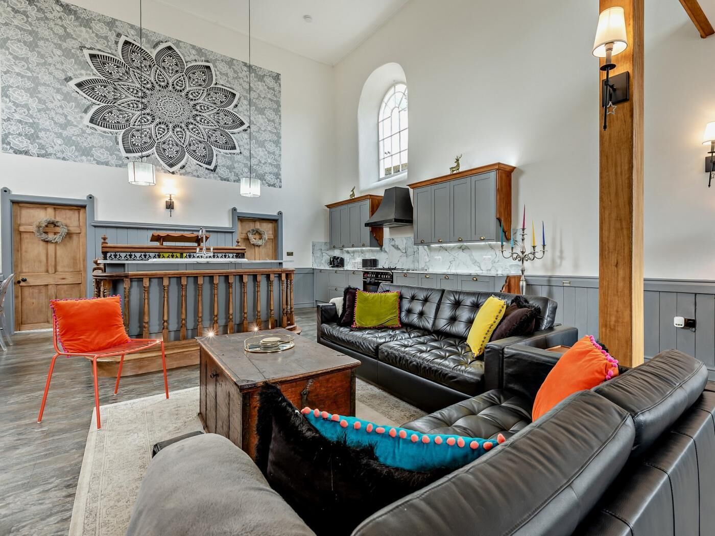 A spacious living area with a large black leather sofa, a wooden dining table, and a kitchen in the background.