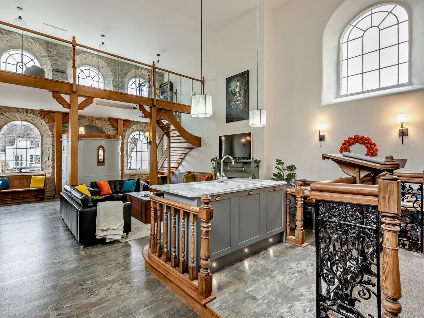 A spacious living area with a high ceiling, a wooden staircase, and a kitchen island.