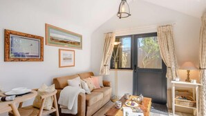A cozy living room with a sofa, a coffee table, a dining table with chairs, a floor lamp, and a window with curtains. - 1 Bed in Wareham (oc-87150) (Ridge)