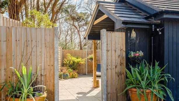 A wooden gate leading to a patio area with potted plants and a building with a dark roof. - 1 Bed in Wareham (oc-87150) (Ridge)