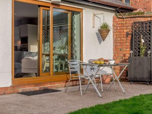 Eine Terrasse mit Tisch und Stühlen, eine Glastür zum Wohnzimmer und eine hängende Pflanze.