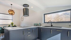 A modern kitchen with a large island, dark cabinetry, and a window with a mountain view.