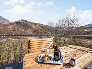 Taula de fusta amb una safata de pastissos i una cafetera, amb vista a un paisatge de muntanyes.