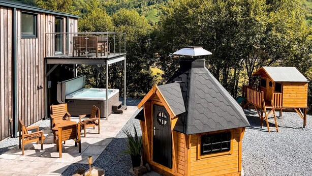 A wooden cabin with a hot tub, outdoor seating, and a small playhouse.