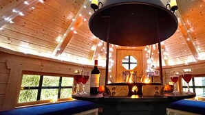 A cozy interior with a central fire feature, wooden walls, and a welcoming sign.