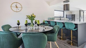 A modern kitchen with a central island, a dining area with green upholstered chairs, and a round table with wine glasses.