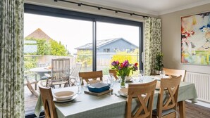 Een eethoek met een tafel voor vier personen, grote ramen en uitzicht op de achtertuin.