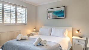 Een slaapkamer met een bed, twee nachtkastjes, een raam met zonwering, een radiator en een schilderij aan de muur.