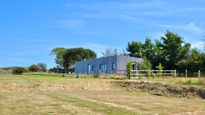 Un edificio moderno con tetto piatto, circondato da un campo recintato e alberi.