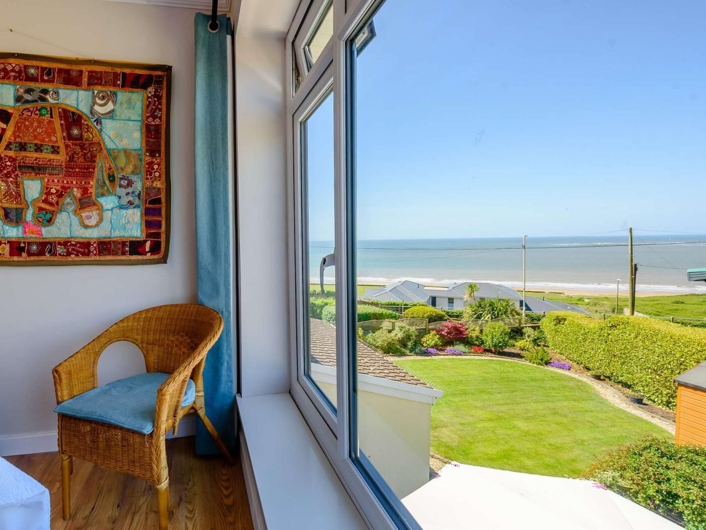 A room with a large window, a wicker chair, and a colorful tapestry.