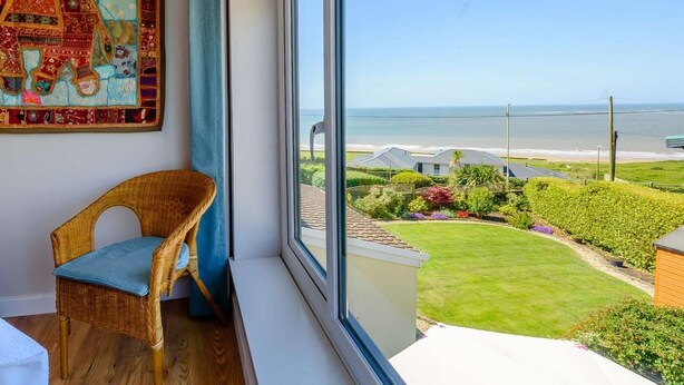 A room with a large window, a wicker chair, and a colorful tapestry. - 4 Bed in Bridgend (oc-87141) (Ogmore-by-Sea)