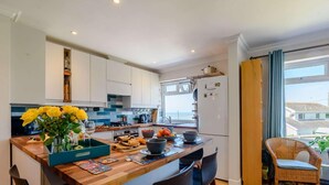 A modern kitchen with white cabinets, a wooden island, and a dining area with black chairs. - 4 Bed in Bridgend (oc-87141) (Ogmore-by-Sea)