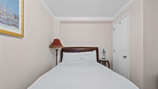 Ein Hotelzimmer mit Bett, Nachttisch, Lampe, Tür und einem Bild an der Wand.