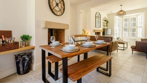 Un comedor con chimenea de ladrillo, una mesa de madera dispuesta para cuatro personas y un gran reloj de pared.