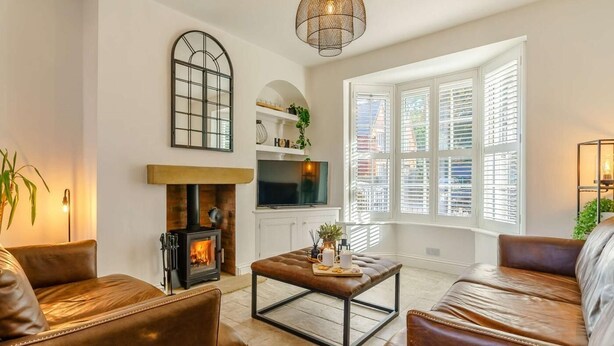 Una sala de estar con sofás de cuero, chimenea, televisor y un ventanal con contraventanas.