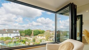 Una habitación con un ventanal grande, una silla blanca y vista a un barrio residencial.