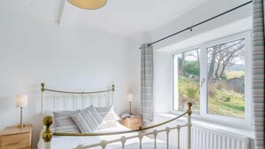 A bedroom with a white metal bed frame, a bedside table, a lamp, a window with a view of the outdoors, and a radiator. - 2 Bed in Ambleside (oc-87180) (Ambleside)