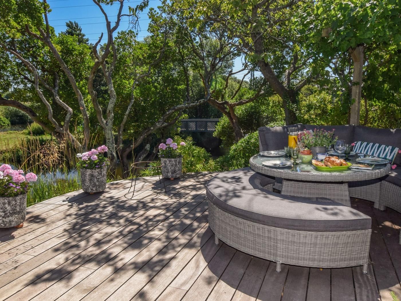 An outdoor dining area with a round table and chairs, surrounded by lush greenery and trees.