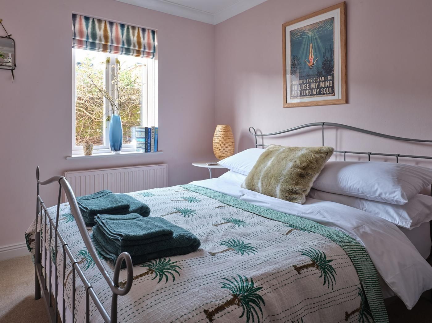 Une chambre à coucher avec un lit, une fenêtre donnant sur des arbres, un tableau encadré au mur et une table de chevet avec une lampe.