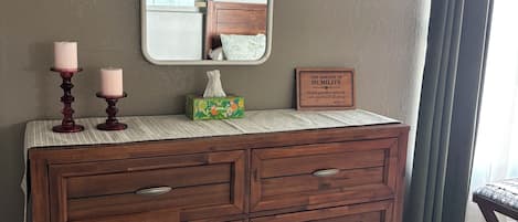 A wooden dresser with drawers, a mirror, and a framed quote on the wall.
