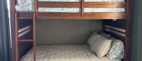 Una cama litera con estructura de madera, un cojín estampado y una colcha color beige.