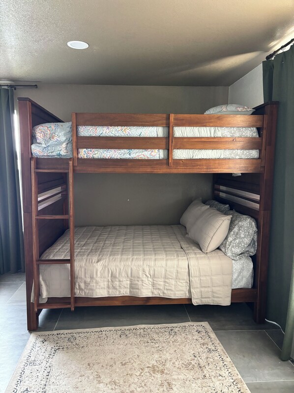 A bunk bed with a wooden frame, a patterned pillow, and a beige quilt.