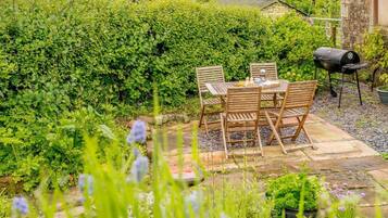 An outdoor patio with a table and chairs, surrounded by lush greenery and a stone pathway.