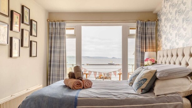 Une chambre avec un grand lit, une vue sur la mer et un balcon équipé d’une table et de chaises.