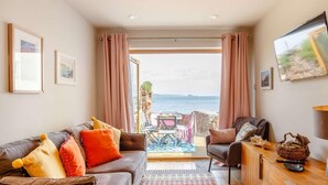 Un salon avec un canapé, des fauteuils, un téléviseur et une vue sur la mer.