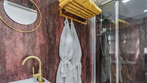 A bathroom with a round mirror, a gold faucet, a white robe, and a glass shower enclosure.