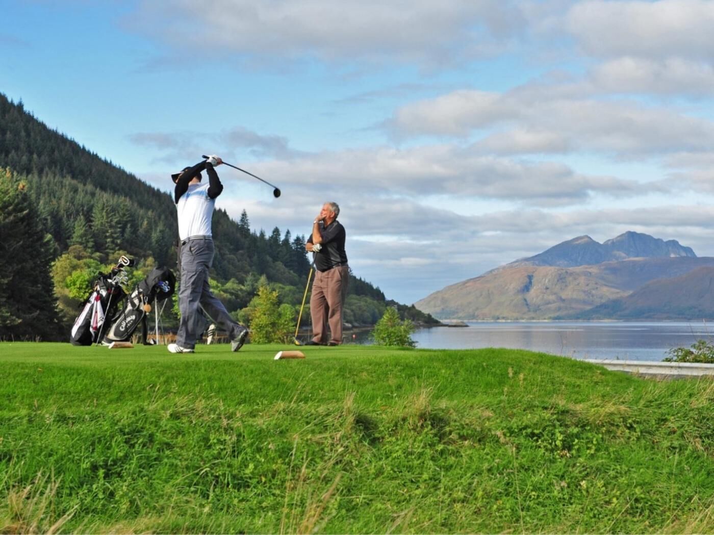 Ein Golfplatz mit See und Bergen im Hintergrund.