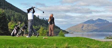 Ein Golfplatz mit See und Bergen im Hintergrund.