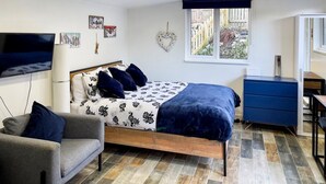 A bedroom with a bed, a TV, a dresser, and a window with a view of a garden.