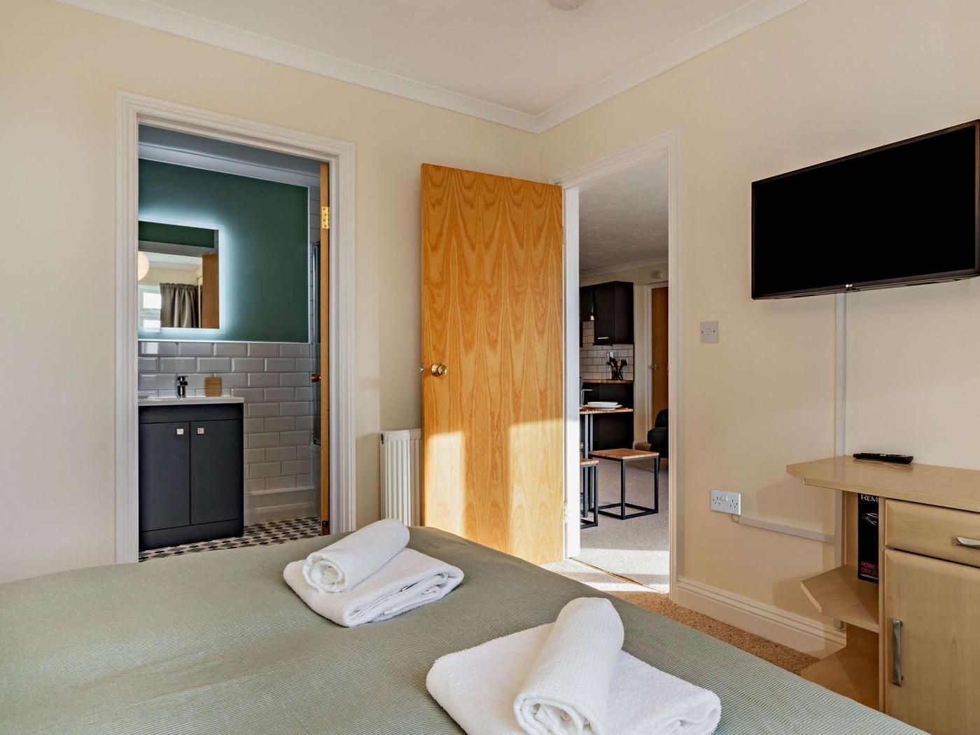 Una stanza con un letto, una televisione, una porta in legno, un bagno e un angolo cottura.