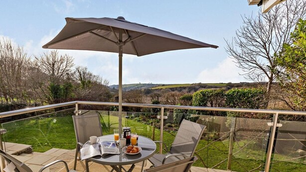 A balcony with a table, chairs, and a large umbrella. - 2 Bed in Bude (oc-87225) (Kilkhampton)