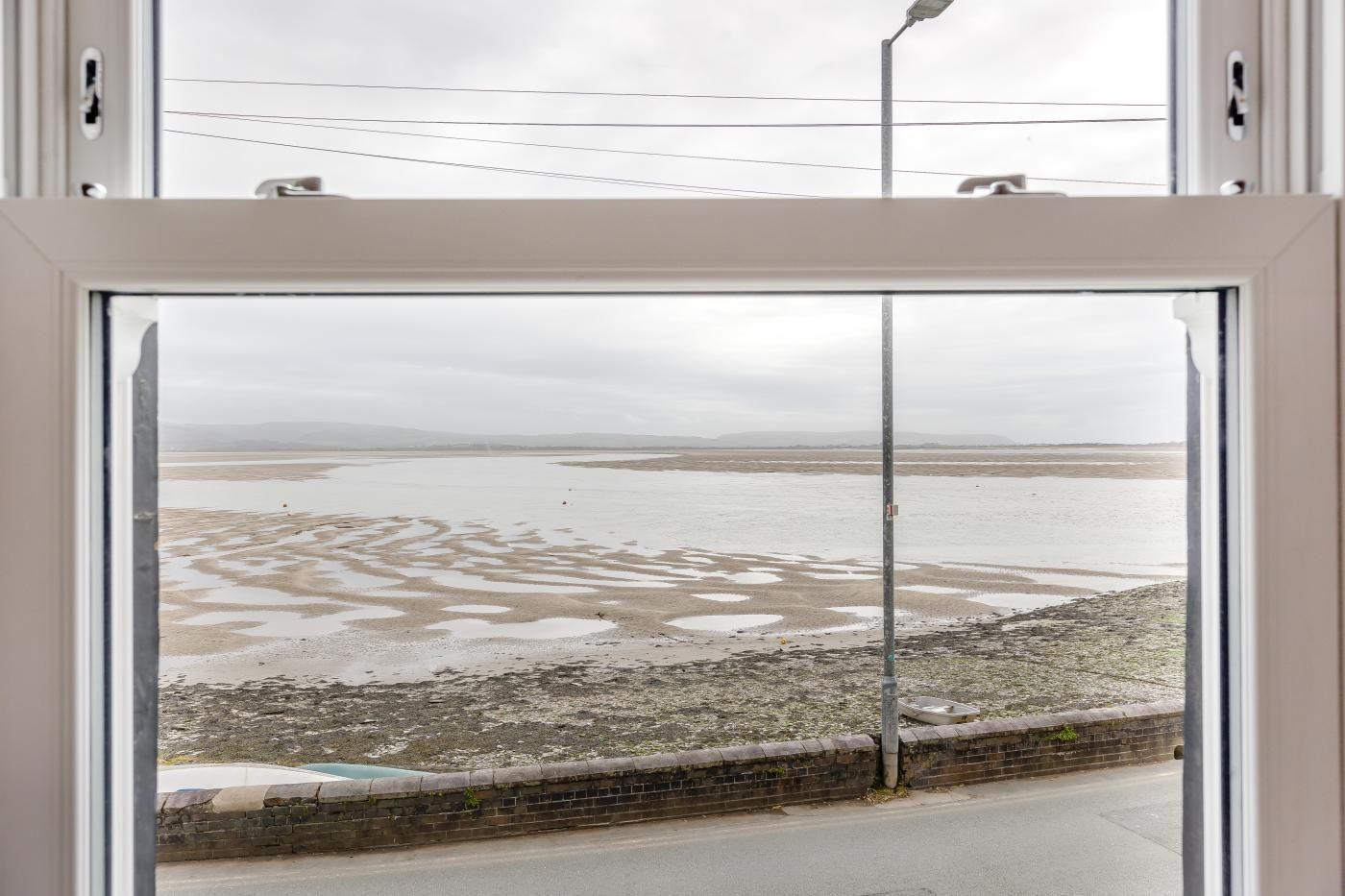 Vista a través de una ventana de un paisaje costero con una carretera y un muro de ladrillo.
