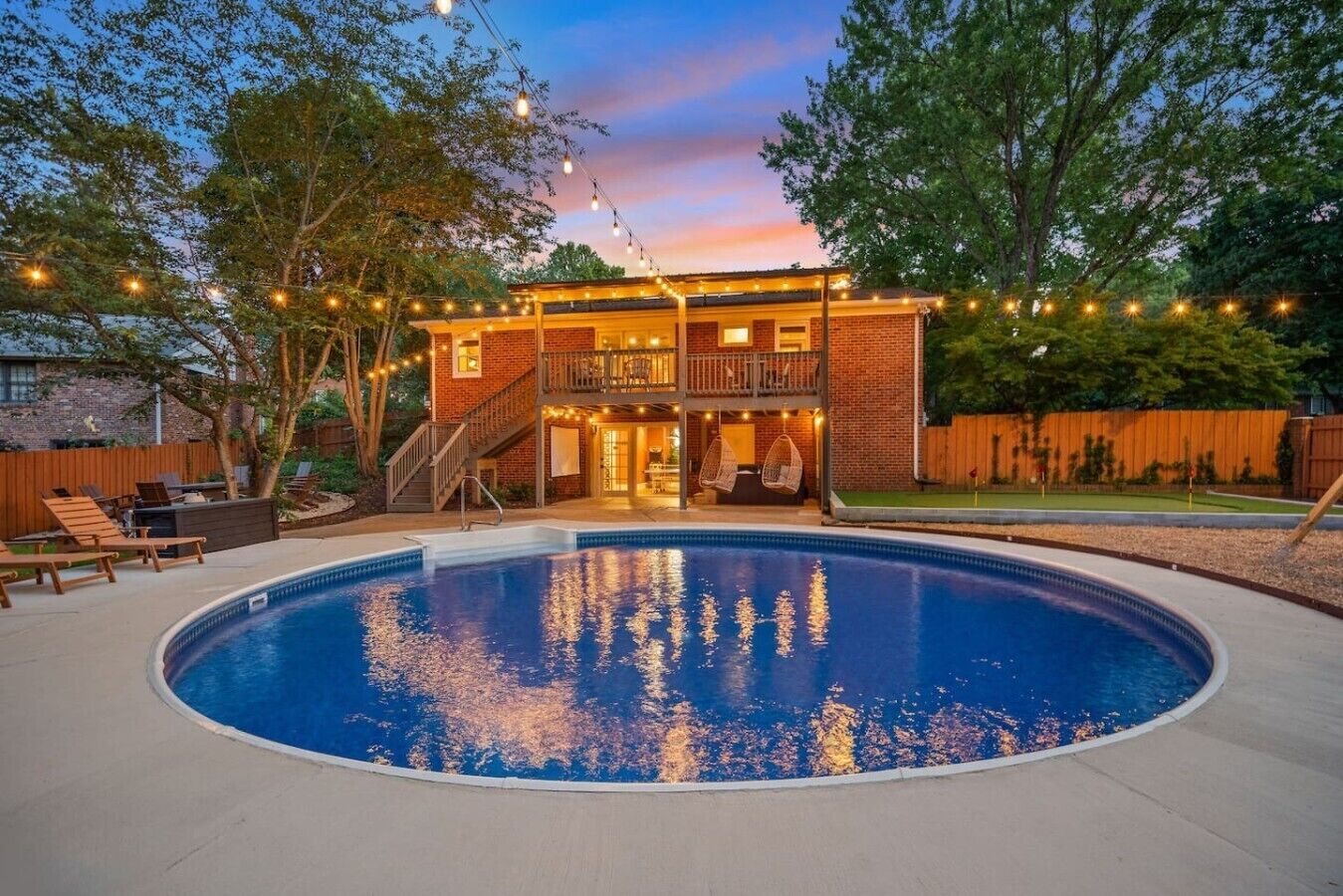 A backyard with a swimming pool, a two-story house, and string lights.