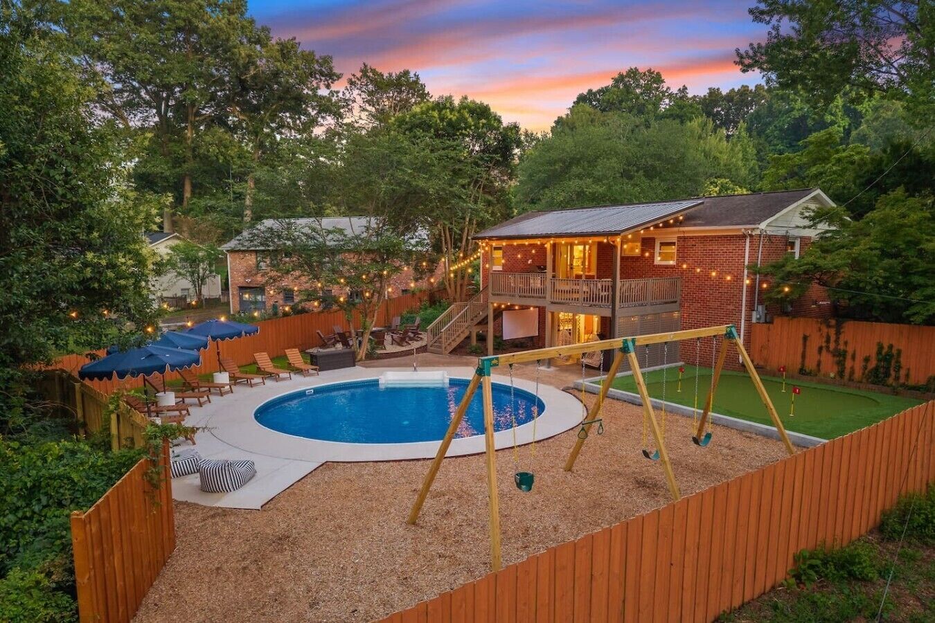 A backyard with a swimming pool, a wooden swing set, and a house with a balcony.